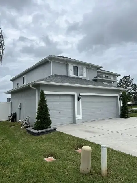 How Does a Seamless Gutter Installation Protect a Two-Story Home in Palm Harbor, FL? Two-story gray house with three-car garage and concrete driveway surrounded by green lawn on a cloudy day