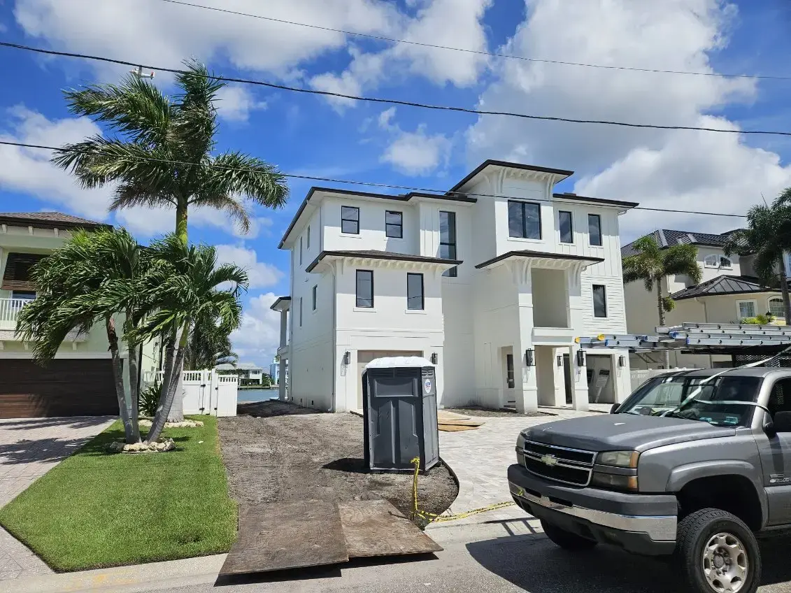 How Does a Residential Drainage System Improve Gutter Performance in Belleair, FL? Three-story white house under construction with a work truck and portable toilet in the palm-lined driveway