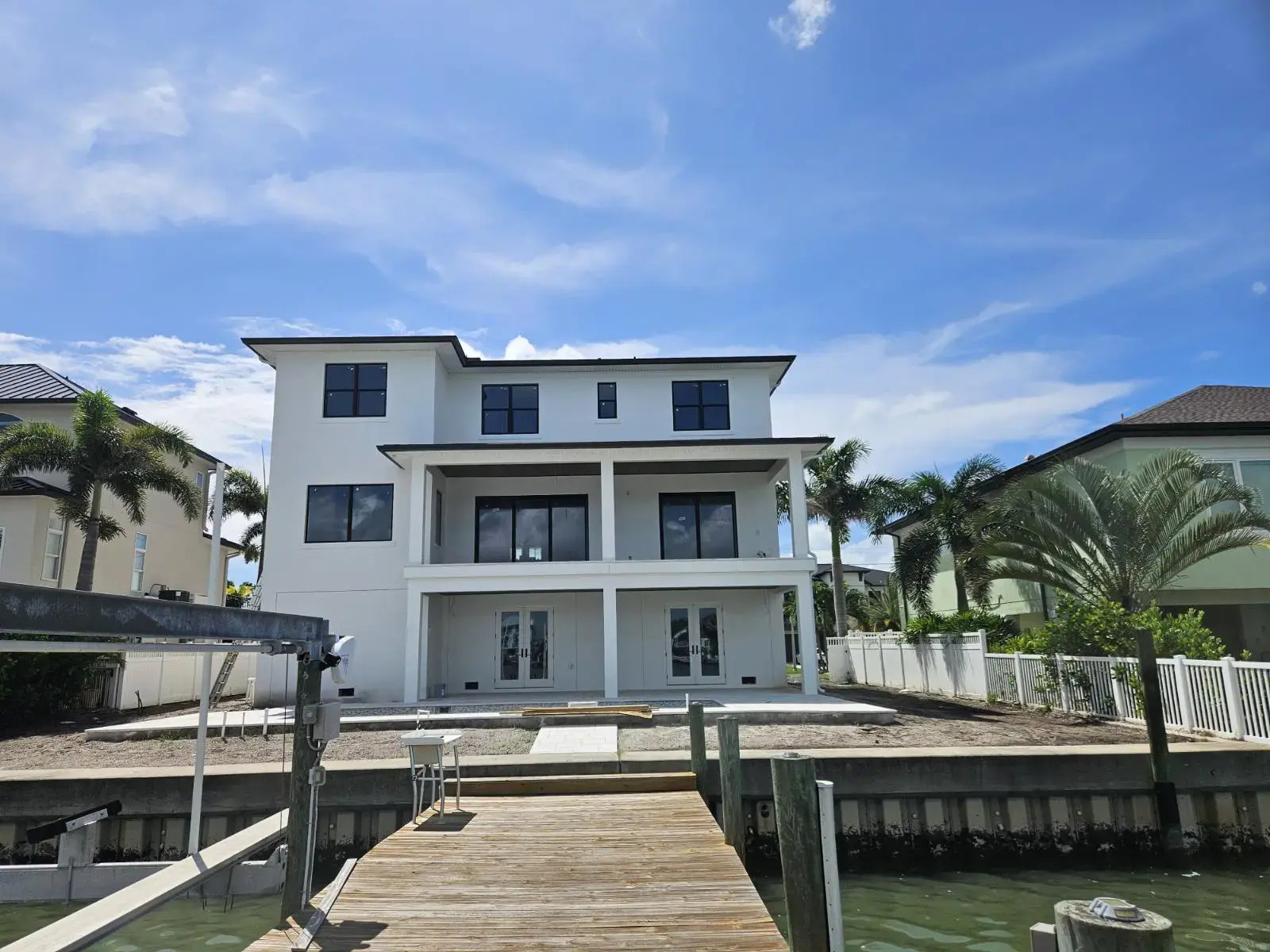 How Does a Residential Drainage System Improve Gutter Performance in Belleair, FL? Modern white three-story waterfront house with a covered balcony, palm trees and a wooden dock