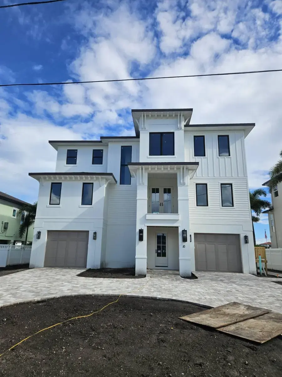 How Does a Residential Drainage System Improve Gutter Performance in Belleair, FL? Modern three-story white house with two garages and a paved driveway under a partly cloudy sky